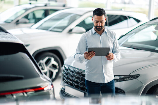 Man using tablet in car dealership surrounded by vehicles