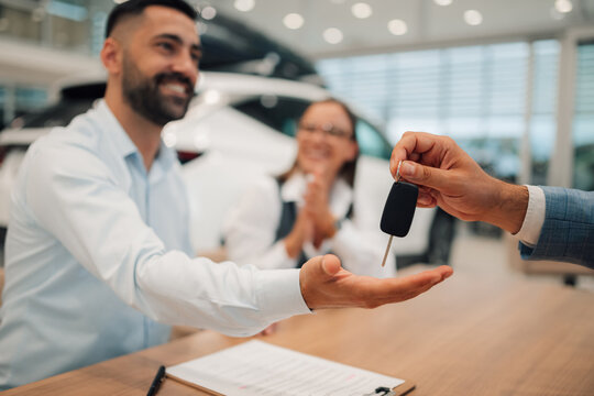 Happy couple receiving car keys from dealer, seated at table.
