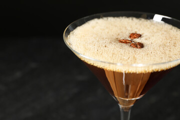 Delicious espresso martini with coffee beans in glass on blurred black background, closeup. Space for text
