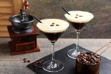 Glasses of delicious espresso martini, manual coffee grinder and beans on wooden table