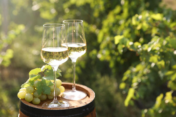 Tasty wine in glasses and grapes on wooden barrel outdoors. Space for text