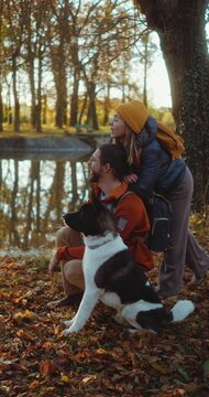 Vertical shot of a  young couple of hikers with their dog enjoying the autumn landscape of nature during a trekking walk by a small lake in the forest