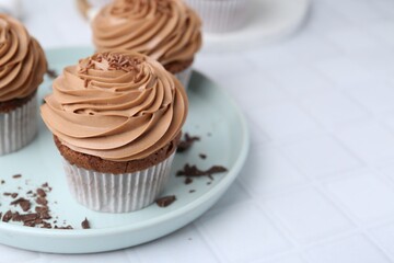 Tasty cupcakes with chocolate cream on white tiled table, closeup. Space for text