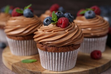 Tasty cupcakes with chocolate cream and berries on brown table, closeup