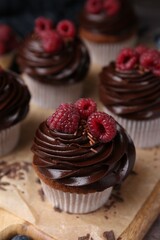 Tasty cupcakes with chocolate cream and raspberries on wooden board, closeup