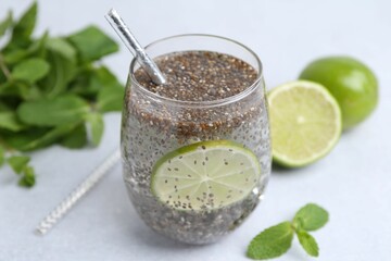 Glass of drink with chia seeds and lime on white table, closeup