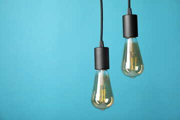 Light bulbs hanging on cords against light blue background, space for text