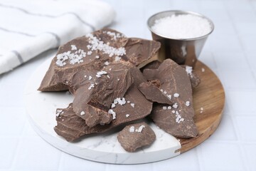 Pieces of tasty chocolate with salt on white tiled table, closeup
