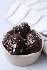 Tasty chocolate candies with salt in bowl on light table, closeup