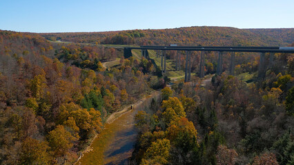 Aerial view of a highway bridge spanning across a river valley with beautiful Fall foliage