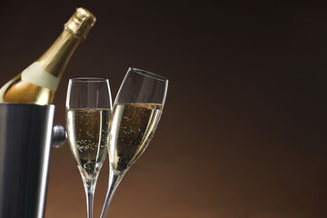 Champagne in glasses and ice bucket with bottle on brown background, space for text