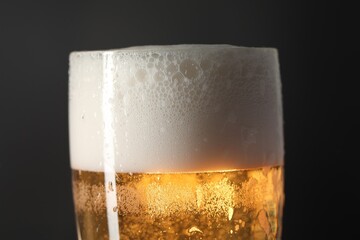 Glass of beer with condensation drops on black background, closeup