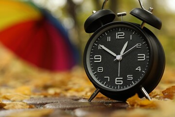 Autumn time. Alarm clock and umbrella in park, selective focus. Space for text