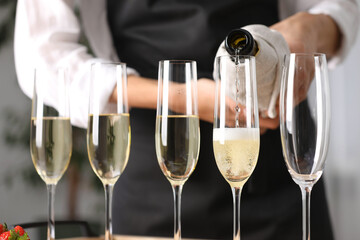 Waiter filling glasses with champagne indoors, closeup