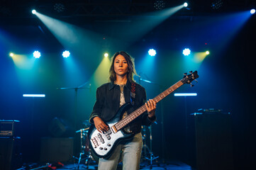 Female musician performing with bass guitar on stage under colorful lights