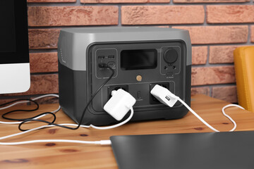 Laptop charging from portable power station on wooden desk indoors