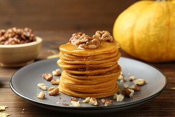 Tasty pumpkin pancakes with honey and walnuts on wooden table, closeup