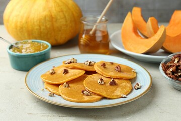 Tasty pumpkin pancakes with nuts, jam and honey on light grey table, closeup