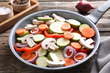 Frying pan with mix of fresh vegetables and mushrooms on wooden table, closeup