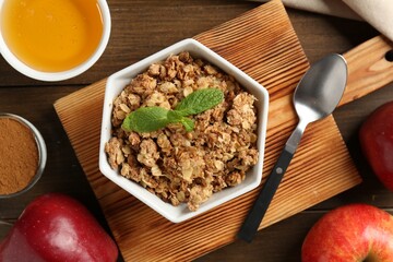 Tasty apple crisp in bowl, ingredients and spoon on wooden table, flat lay