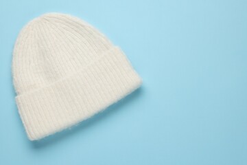 Warm woolen hat on light blue background, top view. Space for text