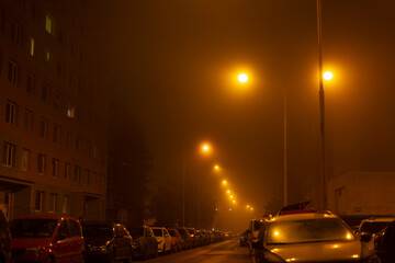 A foggy urban street at night, softly illuminated by streetlamps, showcases a serene atmosphere...