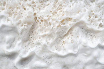 White foam texture on beach waves, soft and bubbly, blending into sandy tones of the shoreline