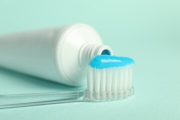 Toothbrush with toothpaste and tube on light blue background, closeup