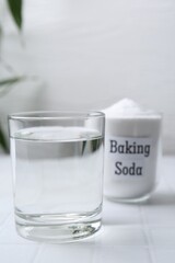 Glass of water and baking soda on white tiled table. Space for text