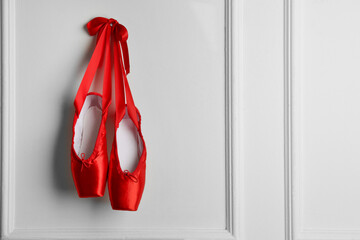 Pair of beautiful red pointe shoes hanging on white wall, space for text © New Africa