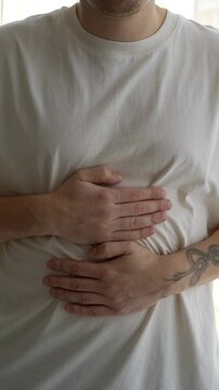 A man has abdominal pain vertical video.
A man holds his stomach with his hands and suffers from severe pain.
A person is constipated from overeating.
A man wants to go to the toilet.
Stomach spasm