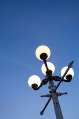 A lantern against a background of clear blue sky with the light on in the evening.