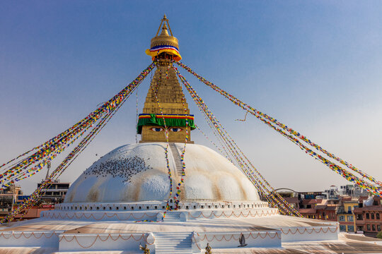 Kathmandu Buddhist stupa Boudhanath. Large spherical stupa in the capital of Nepal UNESCO World Heritage site. Colorful Tibetian prayer flags on the top of stupa with Buddha eyes and blue sky