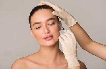 Naklejka premium Plastic Surgery And Beauty Injection Concept. Young Woman Receiving Botox For Wrinkles, Isolated Over Studio Wall