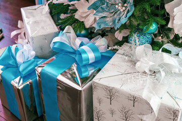 Gleaming gifts wrapped in silver and white paper with blue ribbons are arranged beneath a lush...