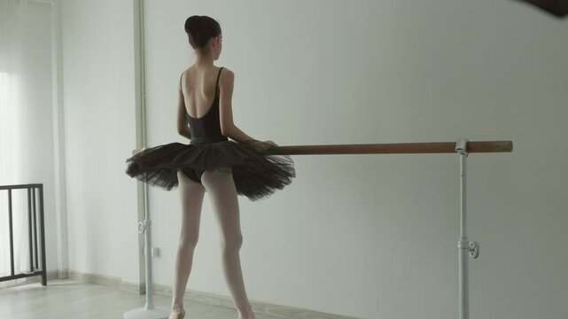Elegant ballet dancer practices at barre in serene studio, showcasing her form in black tutu and pointe shoes, embodying grace and dedication in every movement.