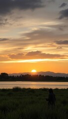sunset over a lake with a person sitting in the grass