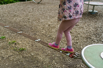 Little cute girl in pink clothes balancing on rope on playground in summer. Healthy active cheerful...