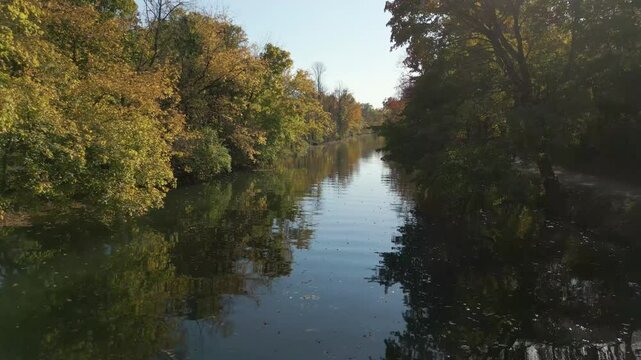 Peaceful river lined with gorgeous Fall foliage during golden hour, drone 4K