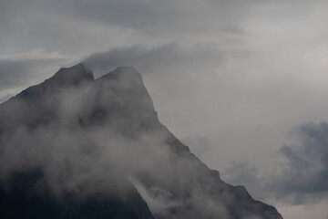 Mysterious looking rocky mountain shrouded in mist and clouds on a gray morning
