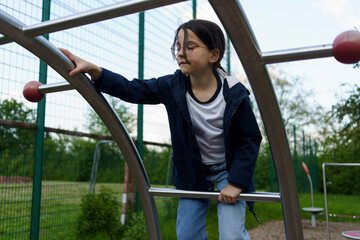 Obraz premium Little cute girl in glasses climbing on playground in summer. Concept of healthy active cheerful child