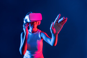Smart female standing with surrounded by cyberpunk neon light wear VR headset connecting metaverse, futuristic cyberspace community technology. Woman using hand touching virtual object. Hallucination.