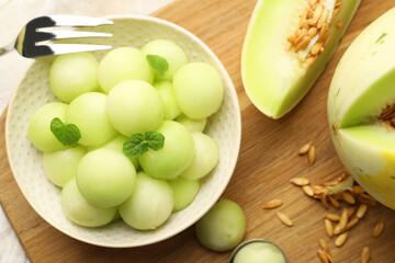 Melon balls in bowl and fresh fruit on wooden board, flat lay