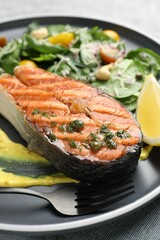 Tasty grilled salmon steak with sauce and salad on table, closeup