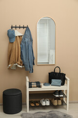 Coat rack with clothes, mirror, shoe storage bench and pouffe in hallway. Interior design