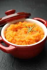 Tasty mashed sweet potato with rosemary in pot on dark textured table, closeup