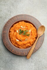 Tasty mashed sweet potato with pumpkin seeds and parsley in bowl served on gray textured table, top view