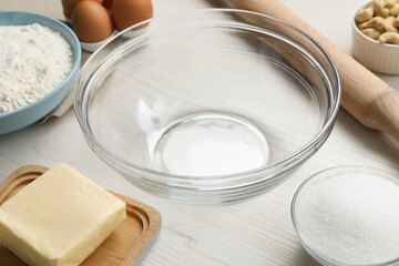Bowl and ingredients for cookies on white wooden table, closeup