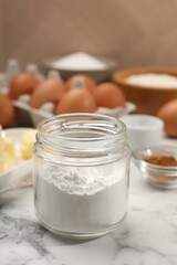 Baking powder in jar and other products on white marble table, closeup