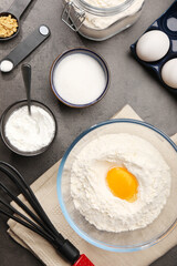 Baking powder with egg yolk in bowl and other products on grey textured table, flat lay